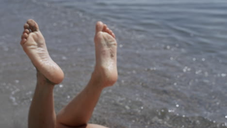 Closeup-woman-legs-waving-in-front-ocean-waves-sunny-day.-Girl-lying-wet-beach.