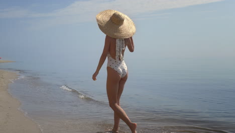 Seductive-girl-stepping-sea-waves-wearing-brimmed-hat.-Woman-walking-seashore.