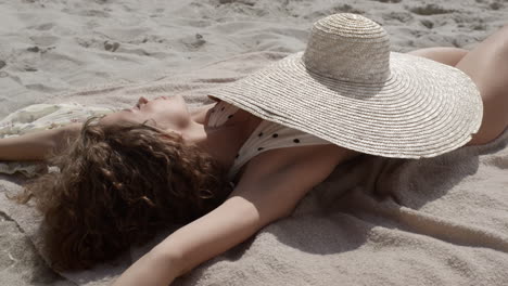Hot-woman-enjoy-sunlight-covering-body-wide-brimmed-hat-on-seashore-close-up.