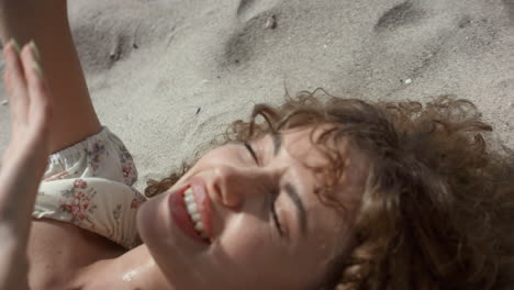 Laughing-cheerful-girl-hiding-from-sun-with-hands-close-up.-Woman-lying-on-sand.