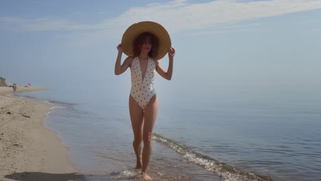 Posh-woman-walk-ocean-water-covering-head-with-brimmed-hat.-Girl-wetting-feet.