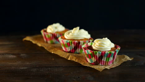Muffins-with-cake-cream-on-baking-paper.-Hand-put-cupcake-on-table