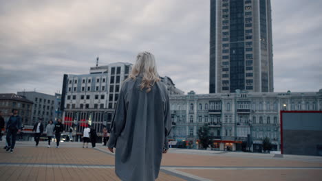 Female-person-walking-city-square-with-urban-buildings-at-evening.