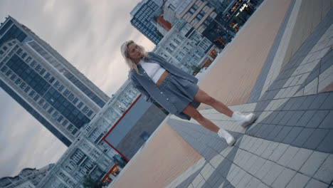 Blonde-model-posing-city-in-evening-on-town-square-modern-buildings.