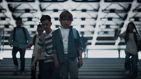 Upset-schoolboy-stand-alone-with-backpack-on-stairway.-Diverse-children-running.