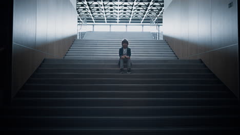 Stressed-schoolboy-stay-alone-on-stairway-close-up.-Boy-hiding-in-school-hall.